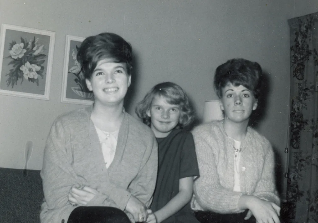 A black and white family photograph from the 1960s: three young people sitting together in a living room.